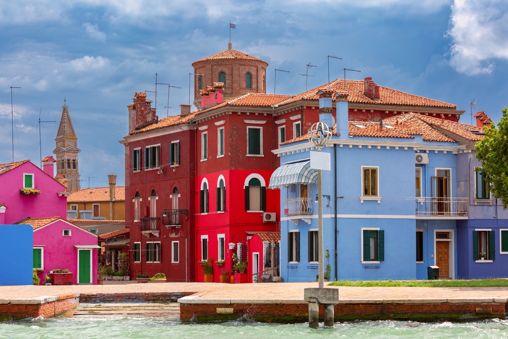 Farverige huse langs en kanal på Burano med kirketårnet i baggrunden