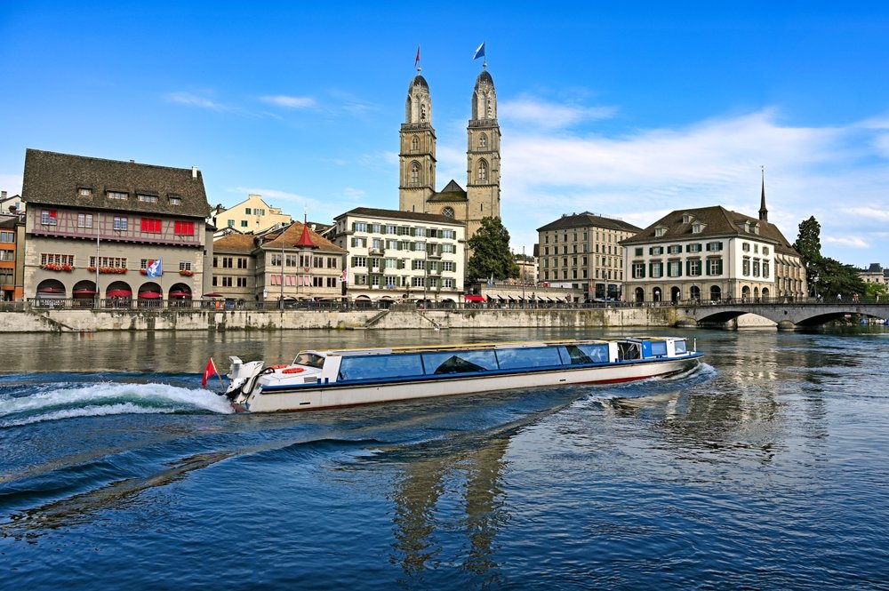 Turistbåd sejler på Limmat i Zürich med Grossmünster i baggrunden