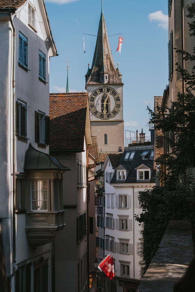 Gade i Niederdorf i Zürich med schweiziske flag og St. Peters tårn i baggrunden